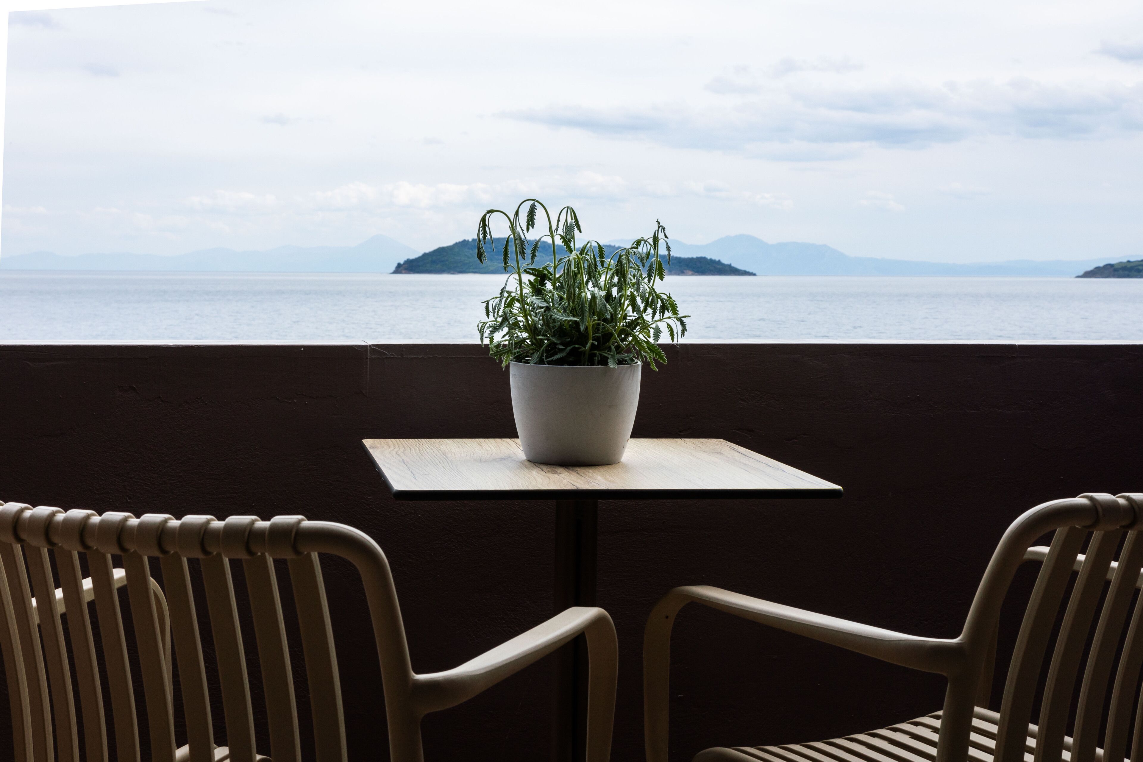 Een balkon met een bloempot, twee stoelen en uitzicht op zee en verre eilanden.