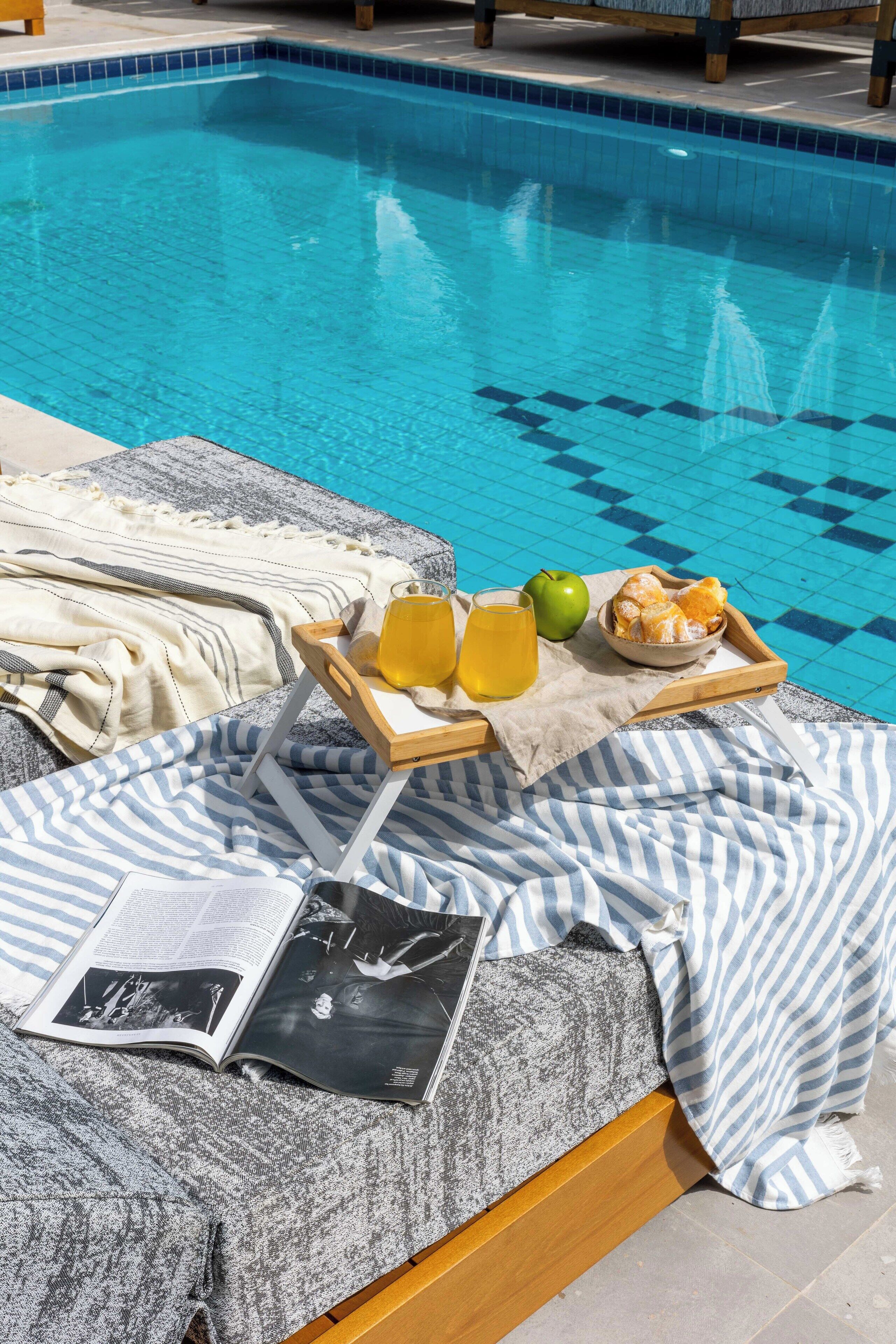 A poolside setting with a towel, a tray with food and drinks, and a magazine.