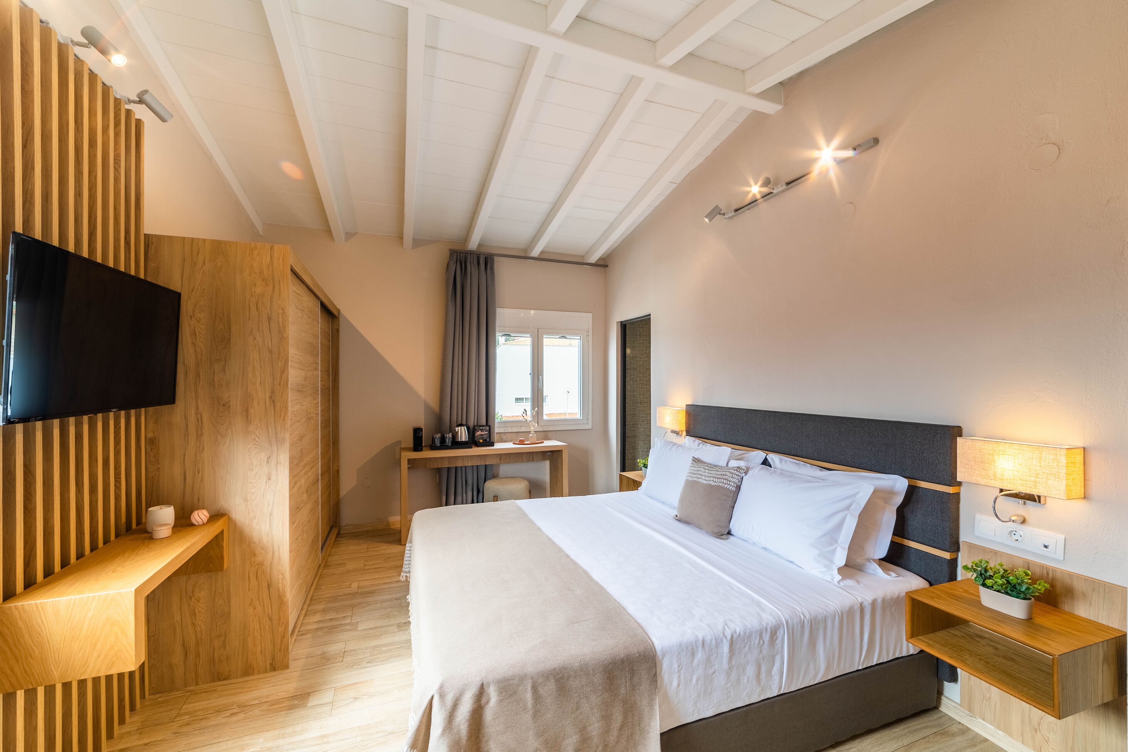 Une chambre moderne avec un grand lit, un téléviseur fixé sur un panneau en bois, un bureau avec une chaise et une fenêtre avec des rideaux.