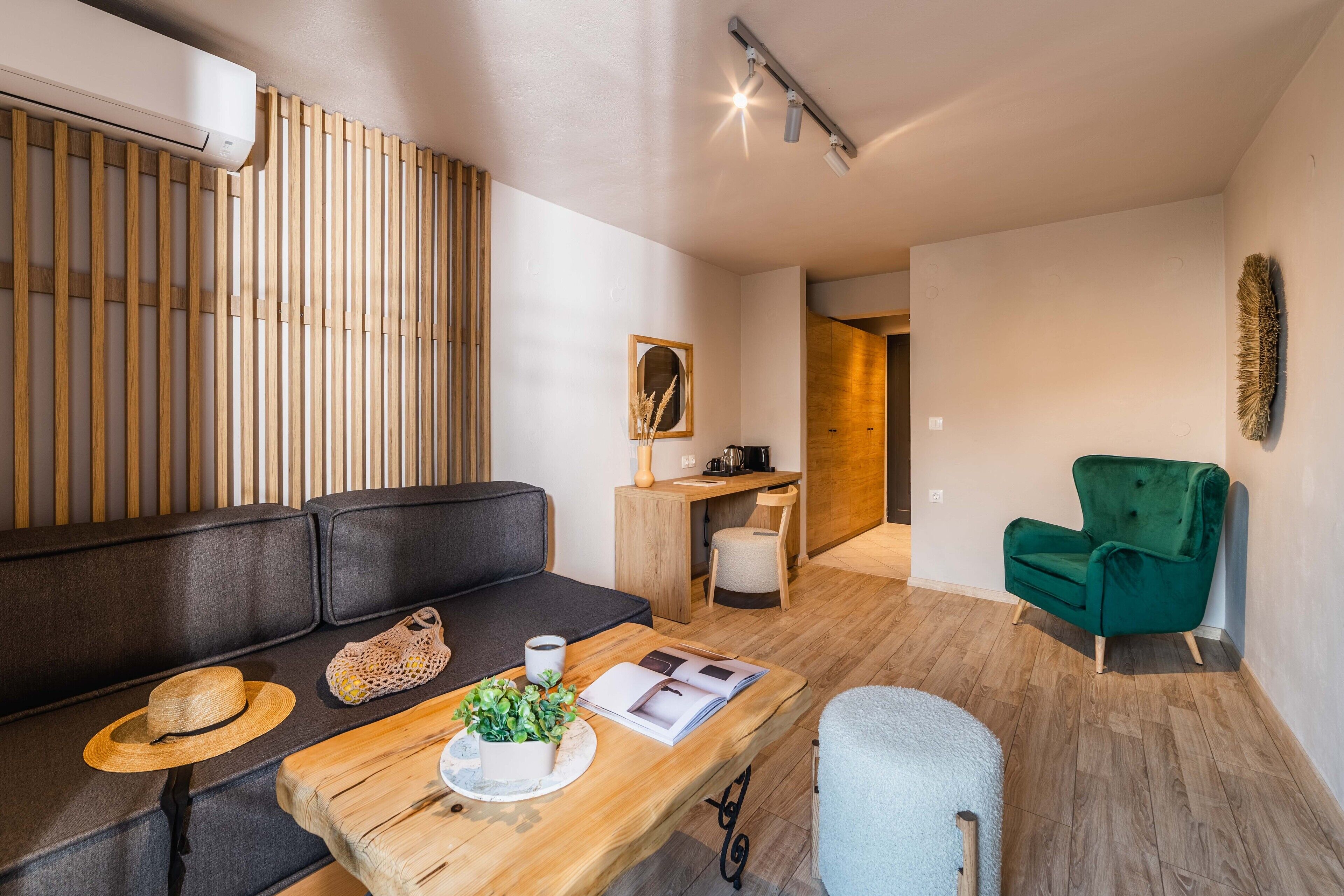 En moderne stue med en væg af trælameller, en sort sofa, et træsofabord med en plante, en grøn lænestol og et skrivebord med stol.