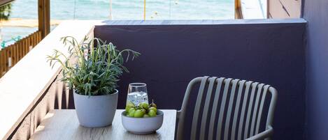 Un balcón con vista al mar, una mesa con una planta en maceta y un frutero, y dos sillas de mimbre.