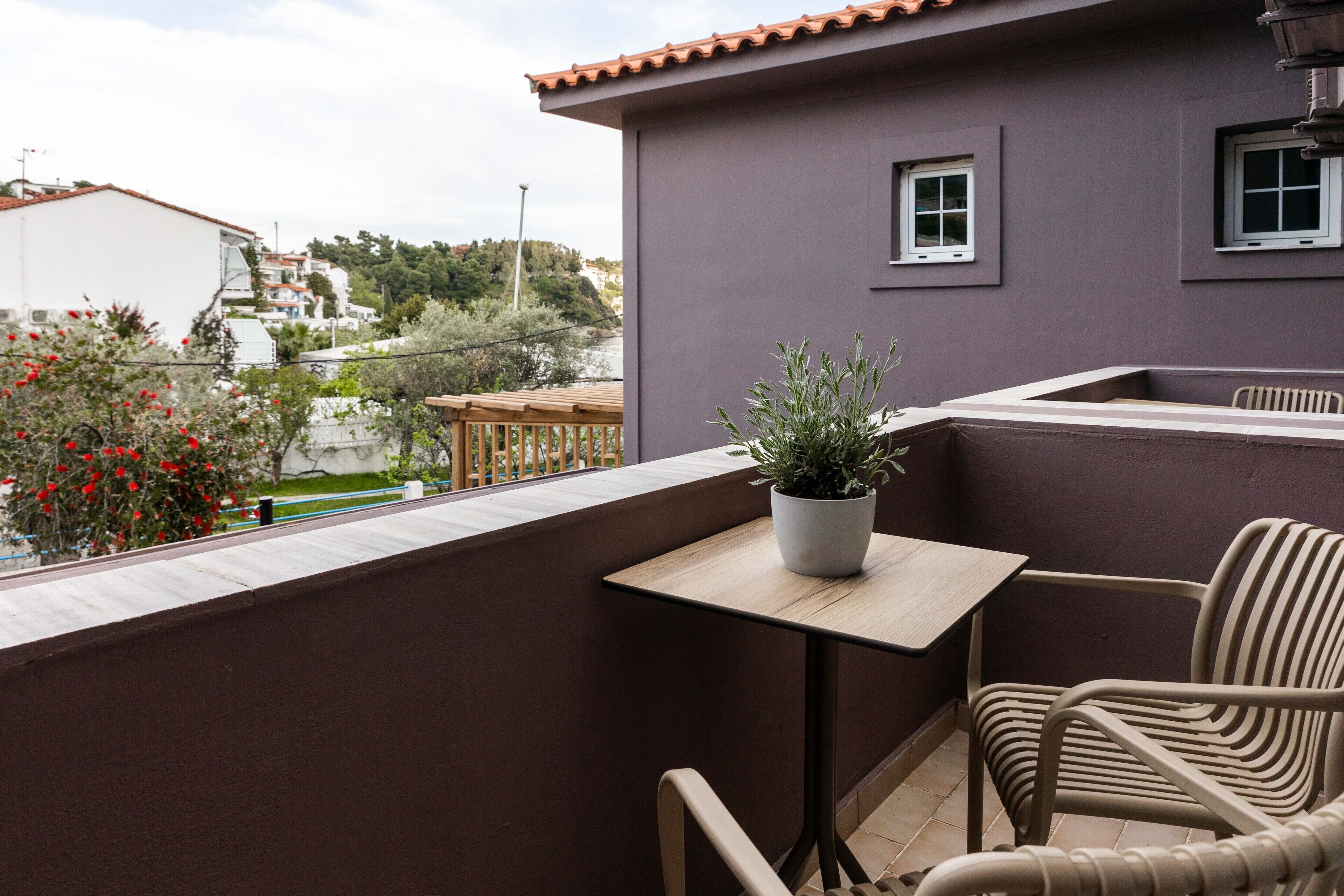A balcony with a table and chairs, a potted plant, and a view of the surrounding neighborhood.