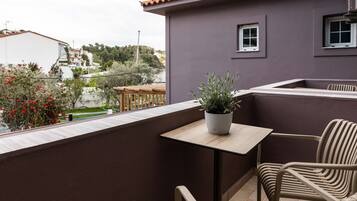 A balcony with a table and chairs, a potted plant, and a view of the surrounding neighborhood.