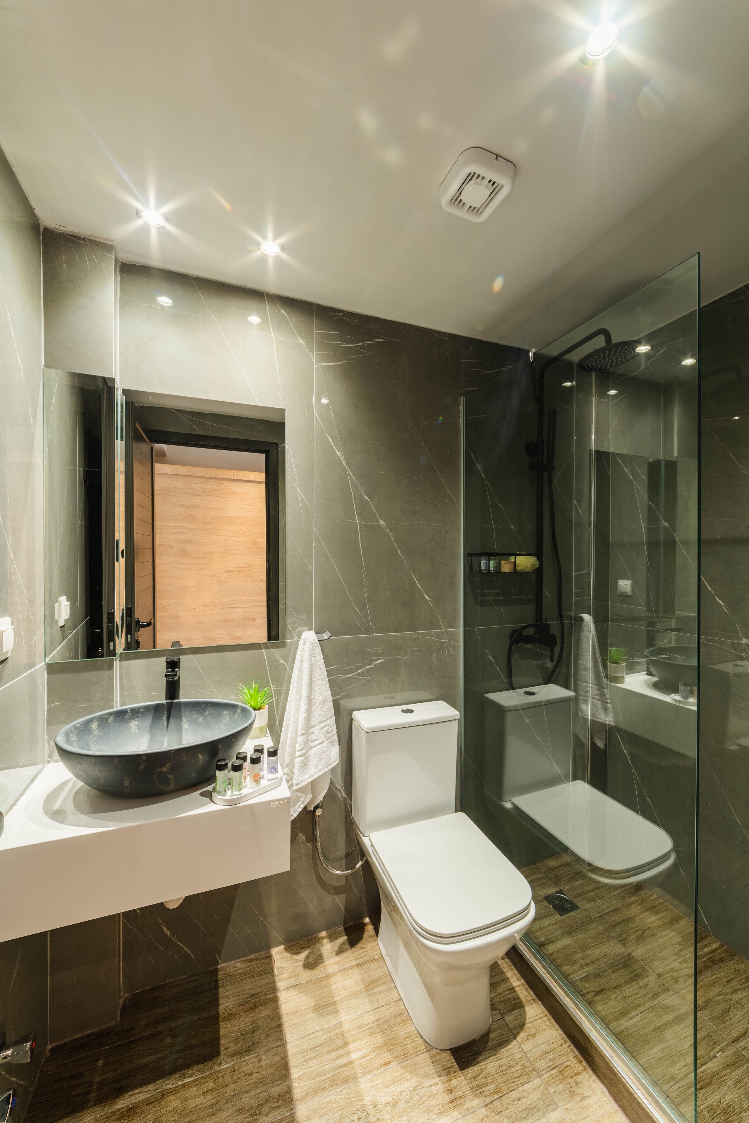 A modern bathroom with a large mirror, a black basin, a white toilet, and a glass-enclosed shower.