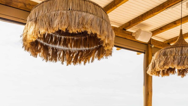 A dining area with a view of the sea, wooden furniture, and hanging thatched lamps. - Thalassa Cape Philian Collection (Skiathos)