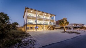 A multi-story hotel with a covered outdoor area, a sandy beach in the foreground, and palm trees.