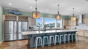 A modern kitchen with stainless steel appliances, a large island with bar stools, and pendant lighting.