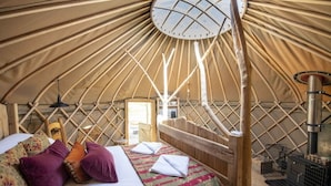 A yurt interior with a bed, pillows, a hanging light, and a wood stove. - Torre Cider Farm (Watchet)