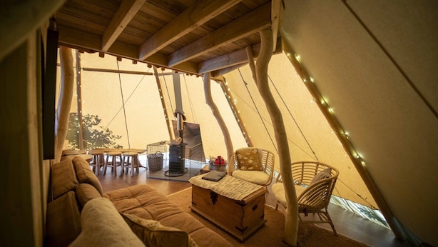 A cozy interior of a tent with a sofa, chairs, a table, and a fireplace. - Torre Cider Farm (Watchet)