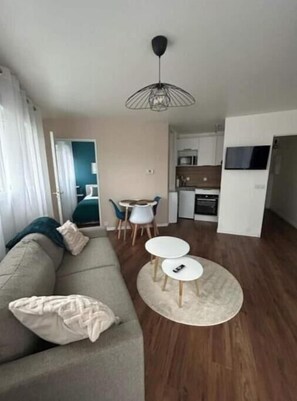 Cozy living space with a sofa, coffee table, and dining area, featuring a flat-screen TV and kitchenette.