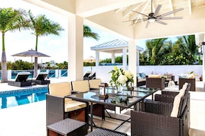 An outdoor pool area with lounge chairs, a glass table, and a ceiling fan.