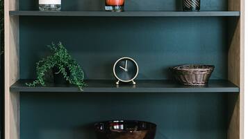 A wooden shelf with various items including a white perforated container, a candle, a small clock, a woven basket, and a clear glass bowl.