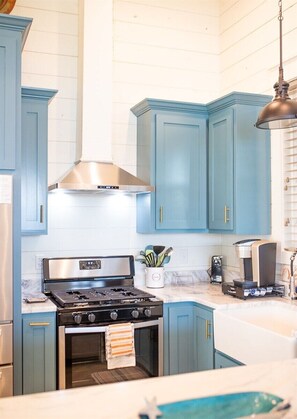 A kitchen with blue cabinets, stainless steel appliances, and a hanging pendant light. - Pelican`s Perch at River Rocks Plantation (Guntersville)