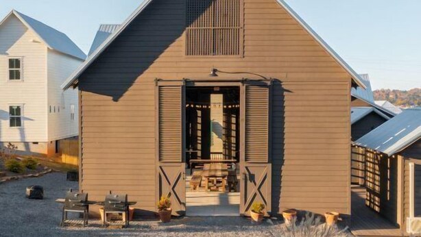 A single-story house with a gabled roof, a front porch with a bench, and a gravel driveway. - Pelican`s Perch at River Rocks Plantation (Guntersville)