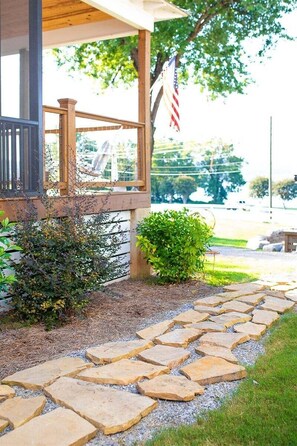A stone pathway leading to a wooden porch with an American flag. - Pelican`s Perch at River Rocks Plantation (Guntersville)