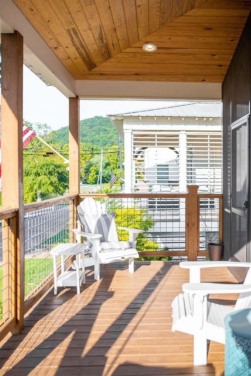 A wooden deck with white chairs and a table, overlooking a residential area with houses and greenery.
