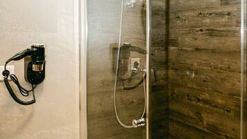 A glass-enclosed shower with a wooden wall panel and a black hairdryer on the wall.