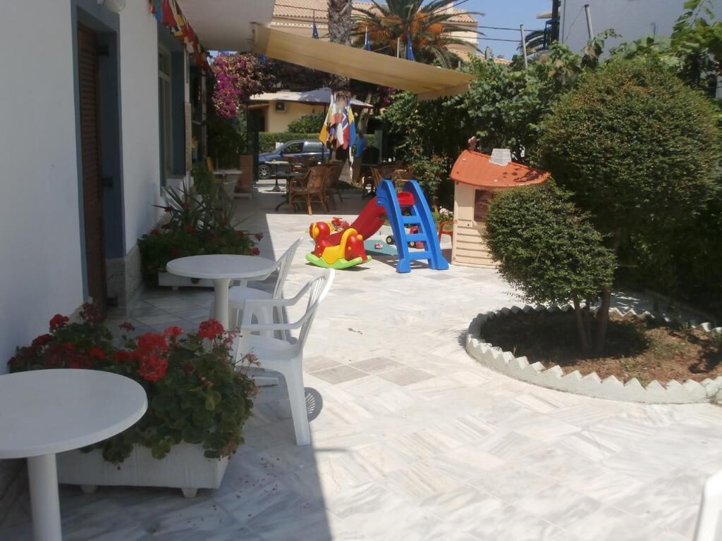 A patio area with a play structure, white plastic chairs, and a small garden.