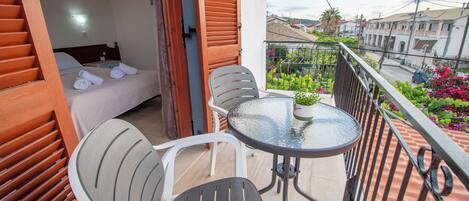 A balcony with a bed, two chairs, a small table, and a potted plant.