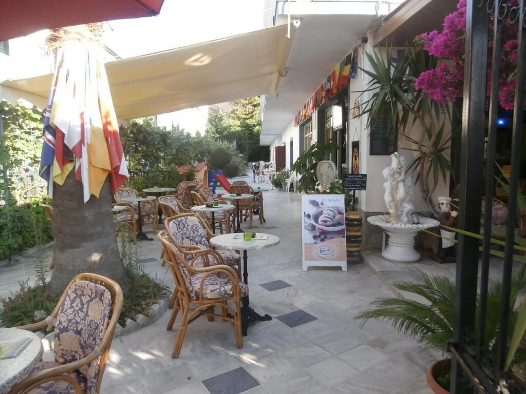 An outdoor cafe area with wicker chairs and tables, surrounded by potted plants and a statue.