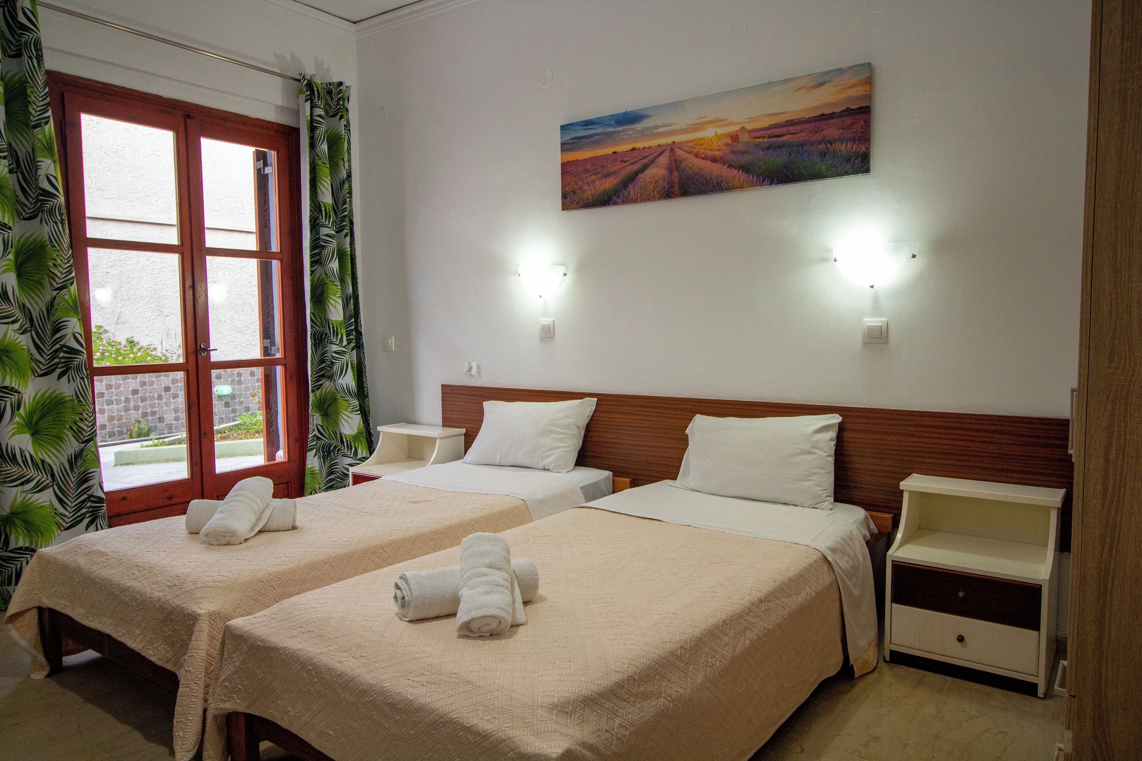 A hotel room with two beds, a painting on the wall, and a window with curtains.