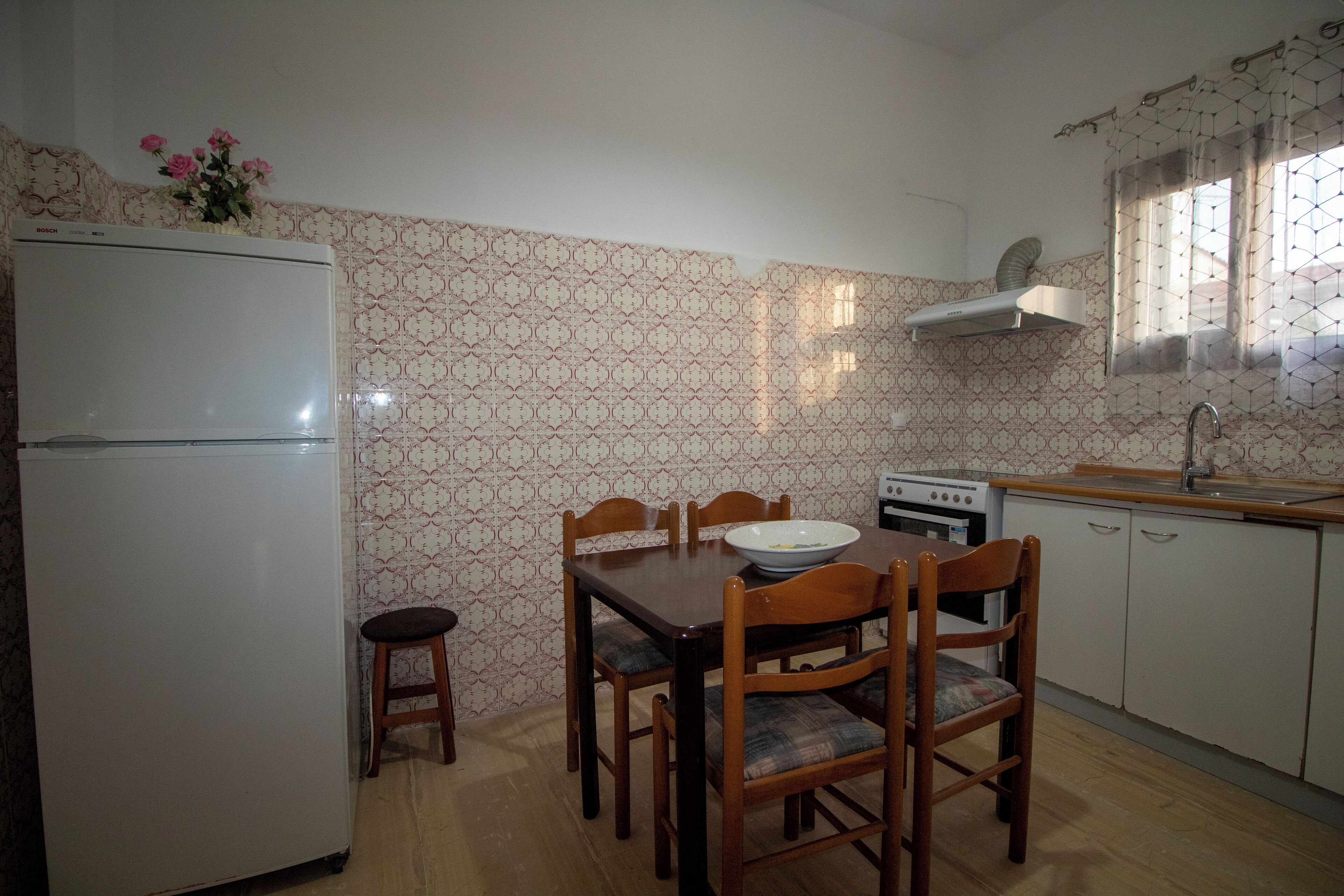 Een kleine keuken met een koelkast, fornuis en een houten eettafel met stoelen.