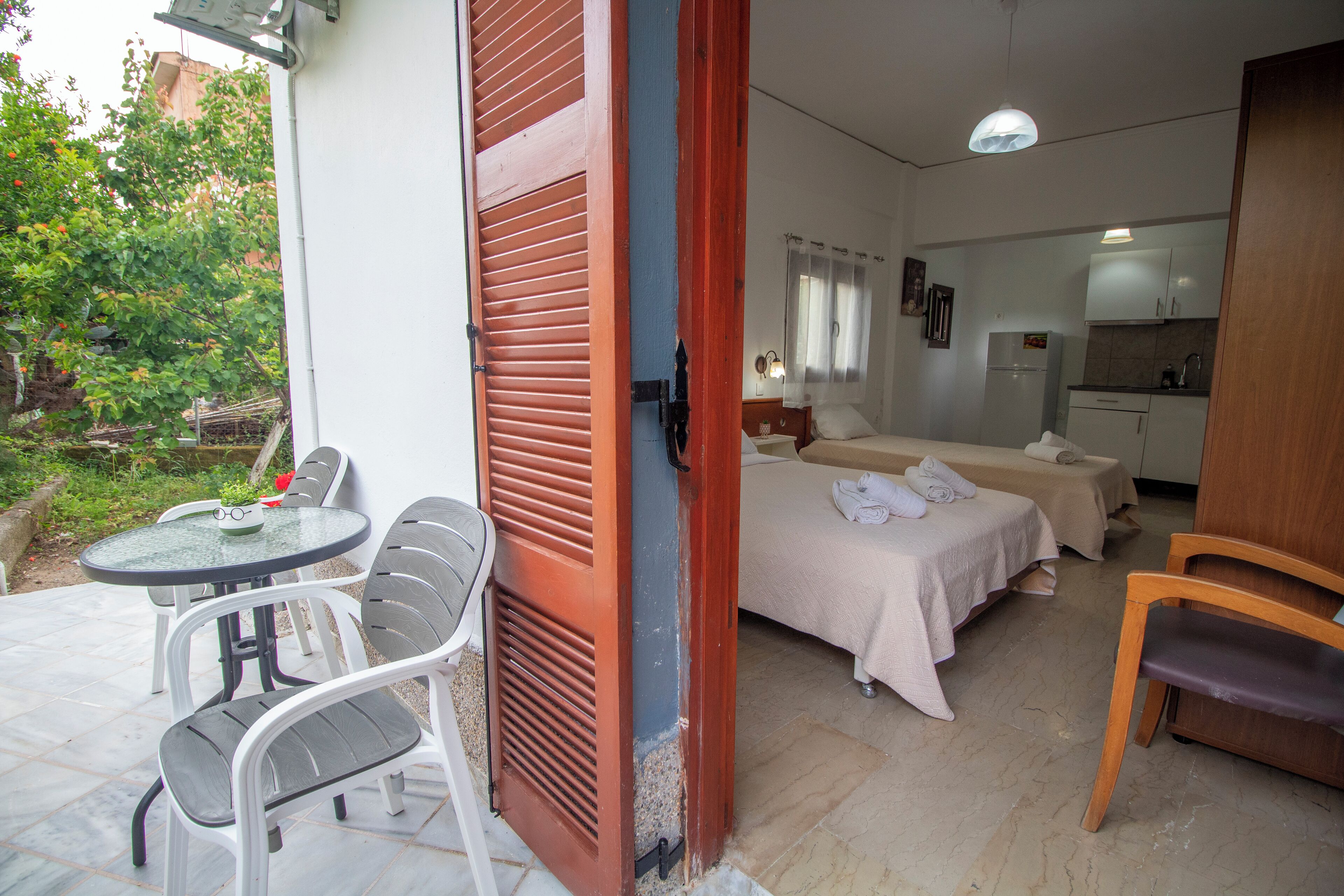 A room with a bed, a small table with chairs, a wooden chair, and a kitchenette area.