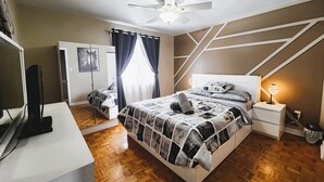 Una camera da letto con un letto, una ventola a soffitto, una lampada da comodino, una televisione e un armadio.