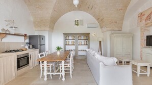 A spacious kitchen with a wooden dining table, white chairs, and a white sofa. There is a built-in oven and a refrigerator. - 3646 Casal 800 by Perle di Puglia (Ostuni)