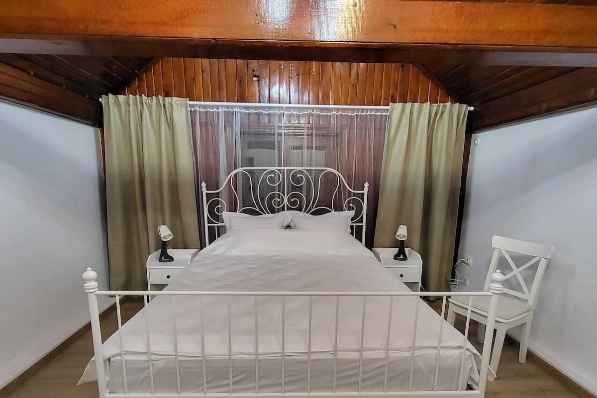 A bedroom with a metal bed frame, a wooden ceiling, and a nightstand with a lamp.
