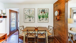 A dining area with a wooden table and chairs, a wooden clock on the wall, and botanical prints above the table. - Mountain Retreat w/ Deck: Near Blue Ridge Parkway (Blowing Rock)