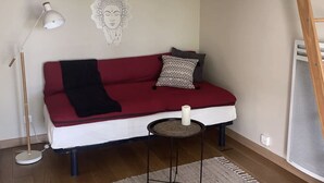 Et hyggeligt rum med en rød og hvid sofa, et lille rundt bord, en gulvlampe og en billeddekoration på væggen.
