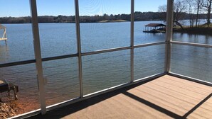 Una terraza cubierta con vista a un lago, un muelle con un bote y una pequeña construcción en la orilla.