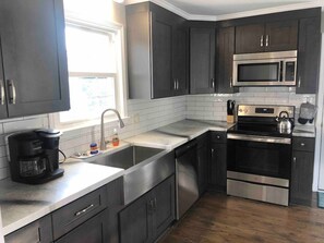 A modern kitchen with dark cabinets, stainless steel appliances, a double sink, and a coffee maker. - 3br/2ba APT, sleeps 7, comfortable and spacious for whole family to spread out (Hickory)