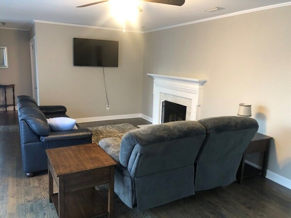 A living room with a fireplace, a sofa, a coffee table, and a TV mounted on the wall. - 3br/2ba APT, sleeps 7, comfortable and spacious for whole family to spread out (Hickory)