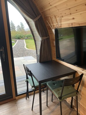 A cozy cabin with a dark wooden table and chairs, a large window, and a flat-screen TV. - Red Squirrel Pod with Hot Tub - perfect for relaxing in countryside near Oban (Oban)
