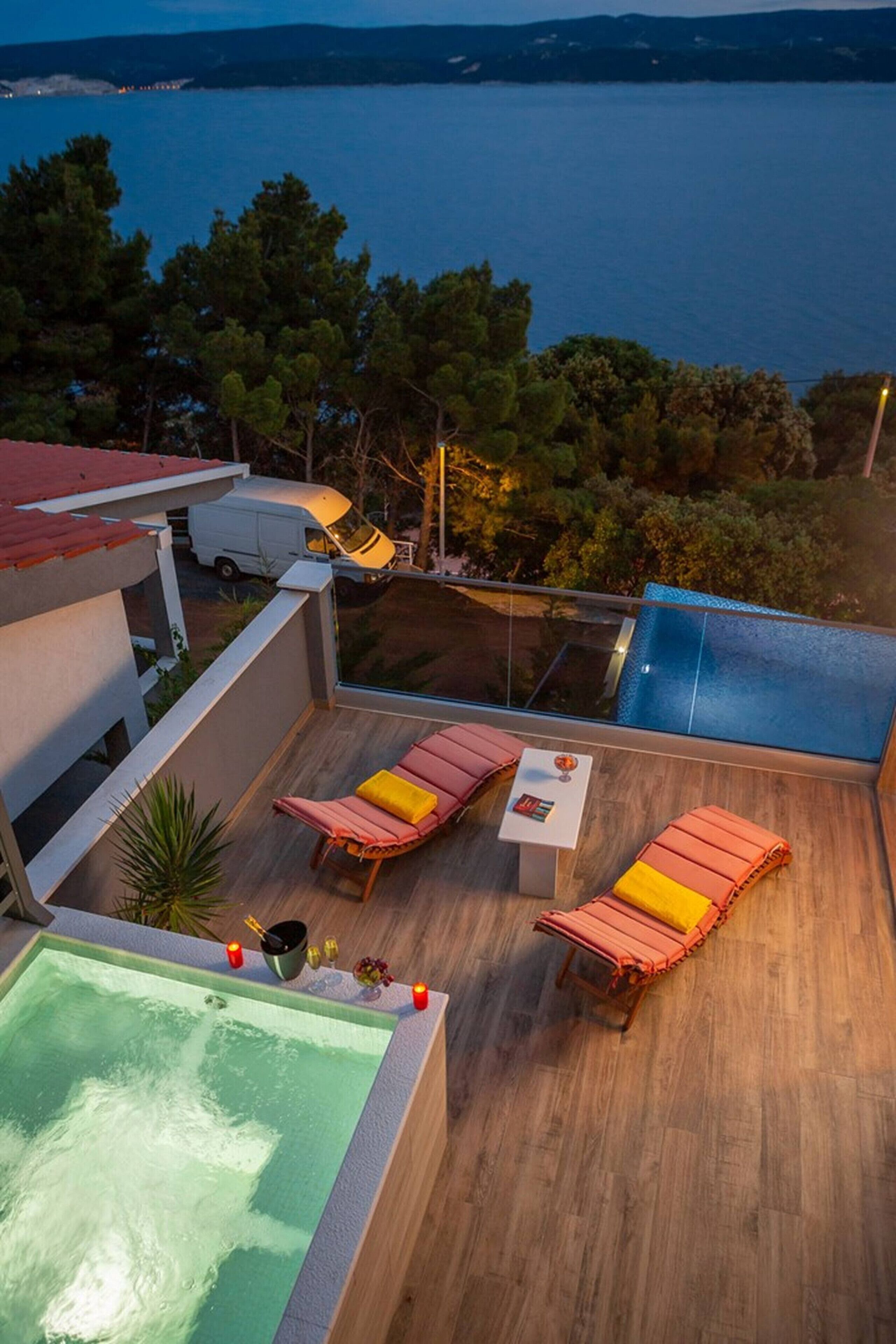 Un espace piscine aménagé sur le toit, avec des chaises longues et une table, offrant une vue sur un plan d’eau et des arbres.
