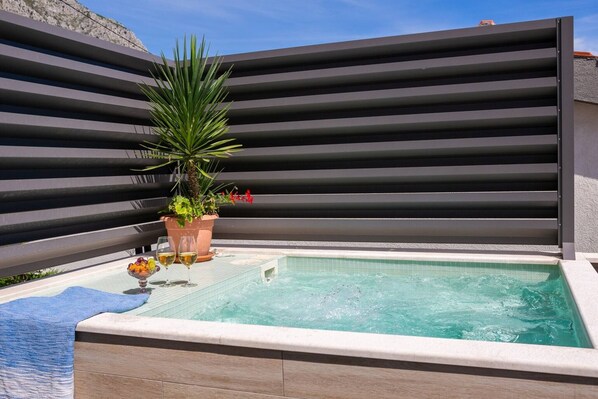Un jacuzzi con borde de azulejos, rodeado por una barandilla moderna y una planta en maceta con flores rojas.