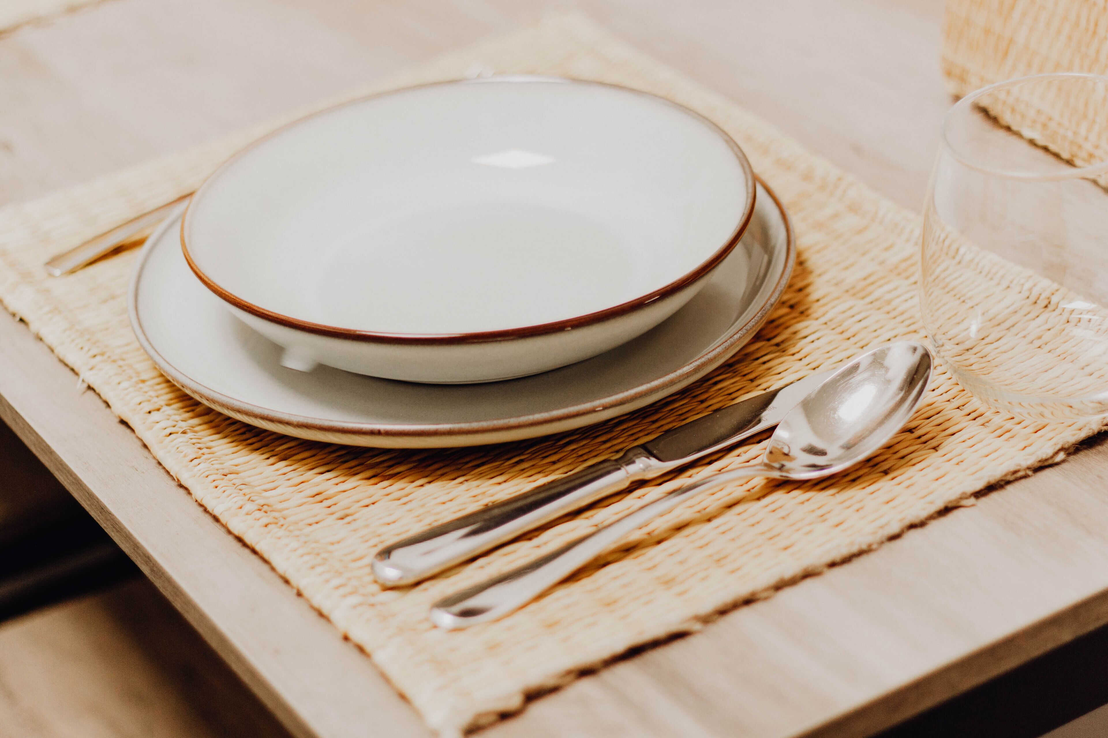 A dining setup with a bowl, plate, spoon, and knife on a woven placemat.