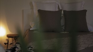 Un dormitorio con cama, almohadas, una mesita y una lámpara.