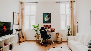 Una sala de estar moderna con un sofá blanco, un escritorio con una computadora, una guitarra y un televisor.