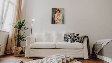 A living room with a white sofa, a painting on the wall, a potted plant, and a floor lamp.