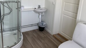 A bathroom with a glass shower enclosure, a sink, a toilet, and a wooden floor. - Tune Hotell Sarpsborg (Sarpsborg)