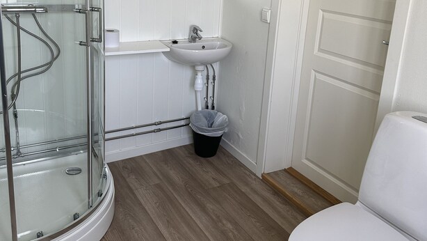 A bathroom with a glass shower enclosure, a sink, a toilet, and a wooden floor. - Tune Hotell Sarpsborg (Sarpsborg)