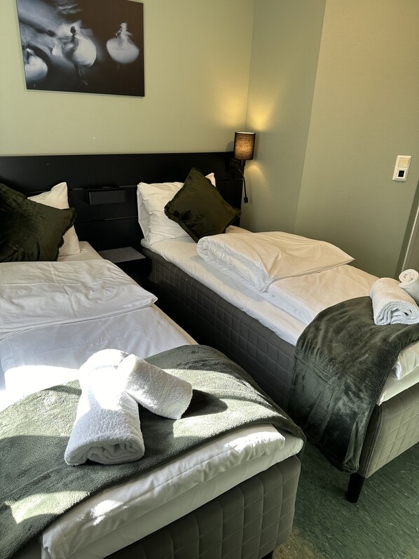 Habitación de hotel con dos camas, una mesita de noche, una lámpara de pared y un cuadro.
