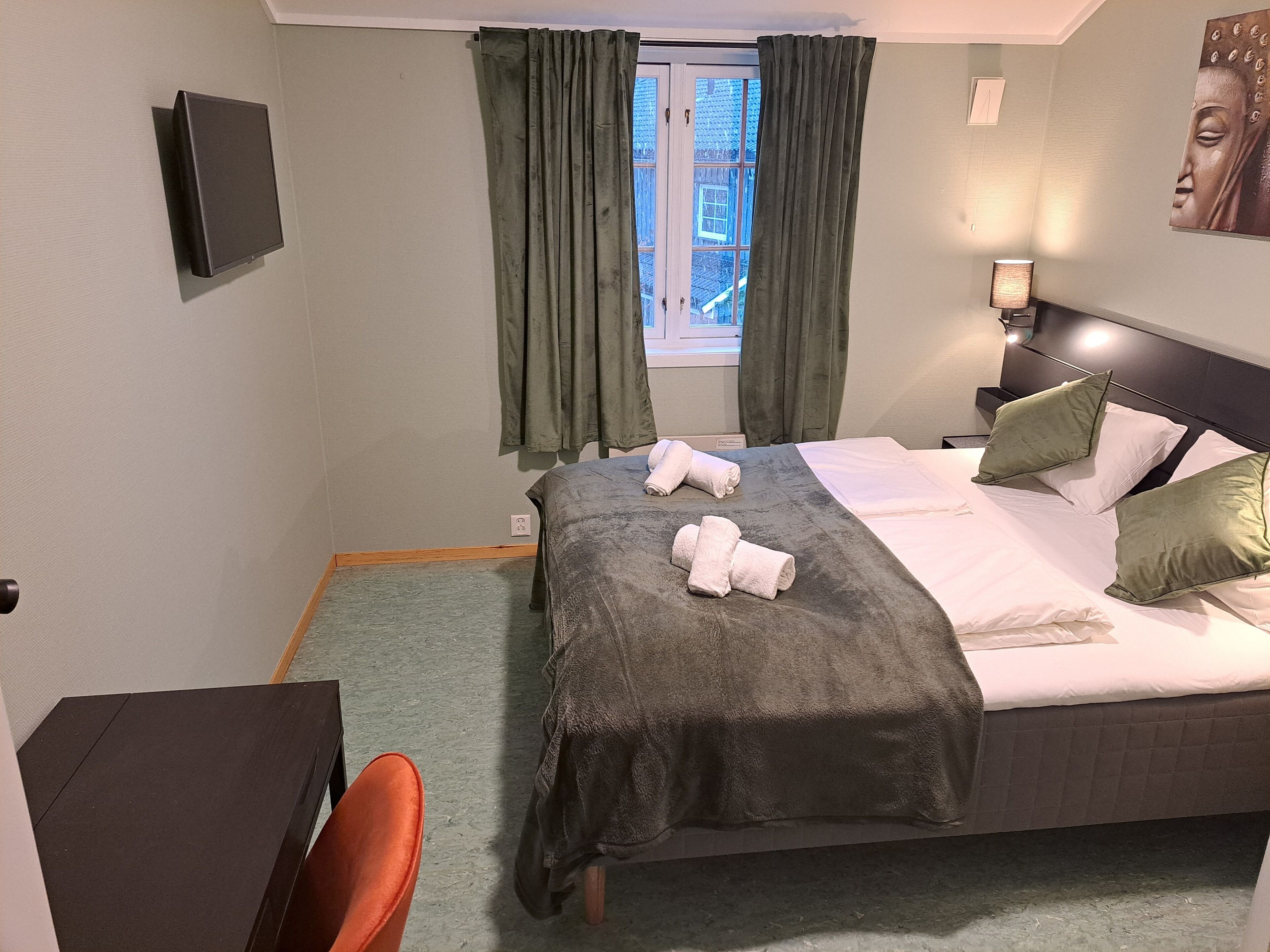 Habitación de hotel con cama, escritorio, silla, televisor montado en la pared y ventana con cortinas.