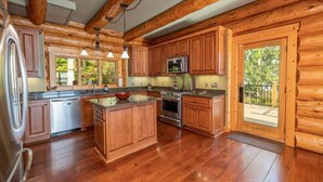 A log cabin kitchen with wooden cabinets, a central island, stainless steel appliances, and large windows. - The Yellowstone | Elegance Meets Lakefront Luxury (Bracey)