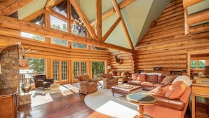 A log cabin interior with a large living area, stone fireplace, and large windows. - The Yellowstone | Elegance Meets Lakefront Luxury (Bracey)