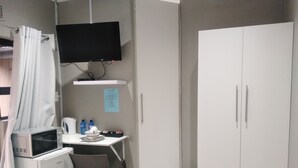 A small, functional room with a desk, chair, microwave, and a TV mounted on the wall. - Nqabanqaba B&B  (Richards Bay)