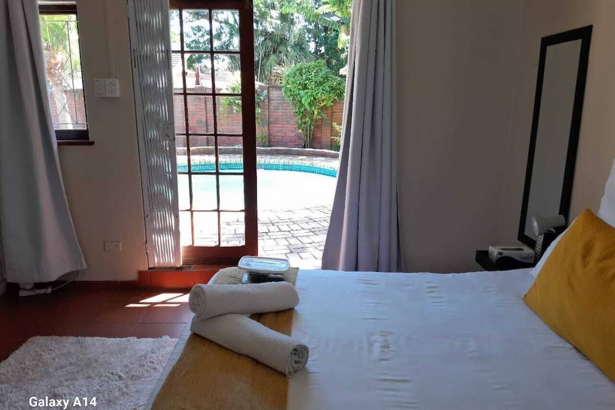 A bedroom with a bed, a white rug, a yellow pillow, and a view of a swimming pool.